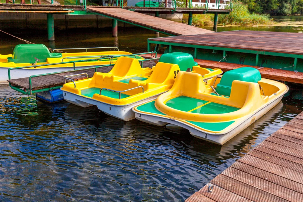 Pédalo blanc à deux places naviguant sur le lac d’Enghien-les-Bains avec vue sur la verdure et les bâtiments thermaux.